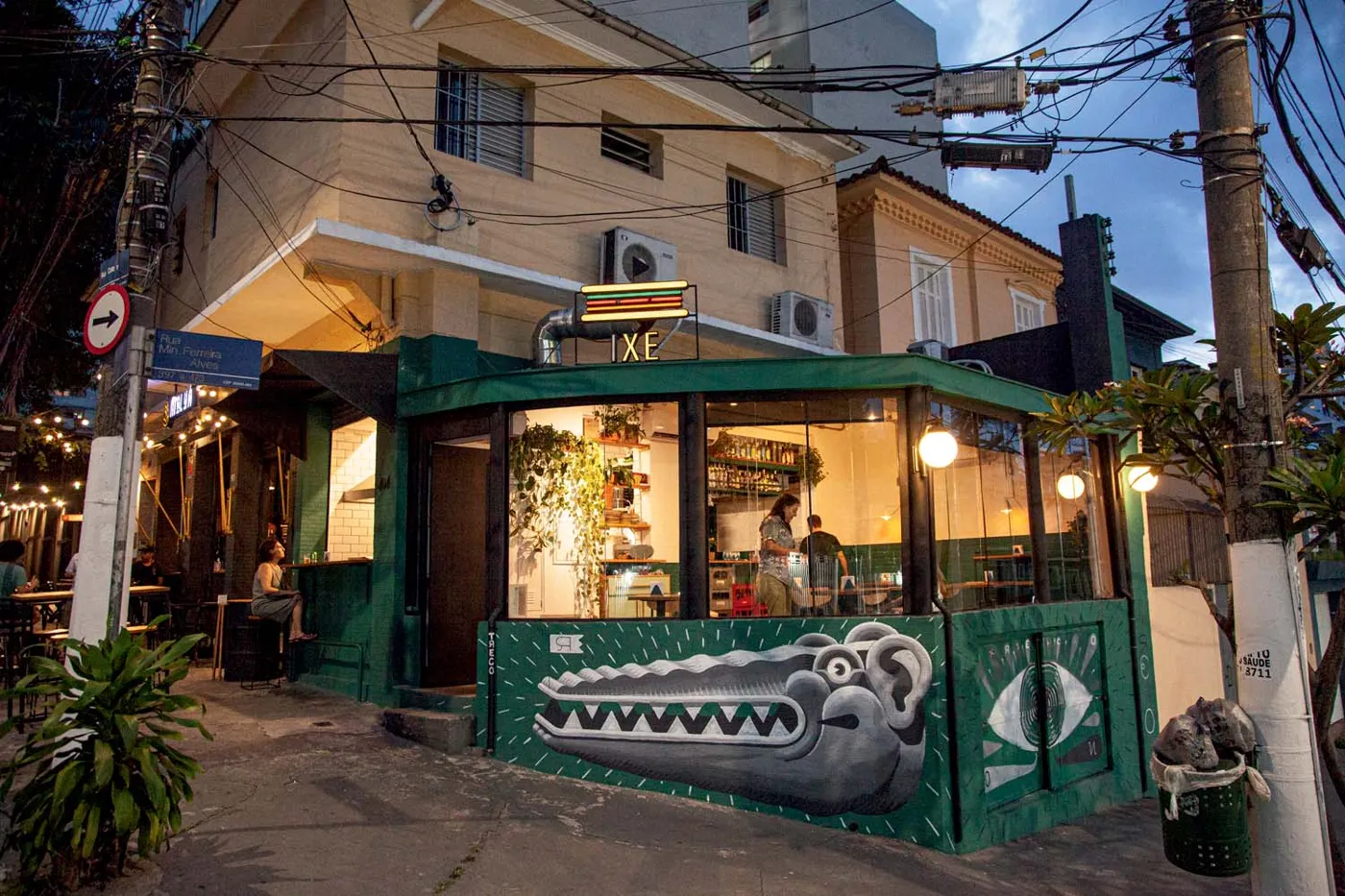 Esquina do IXE na Rua Cotoxó, com fachada verde, janelas grandes e mesas na calçada